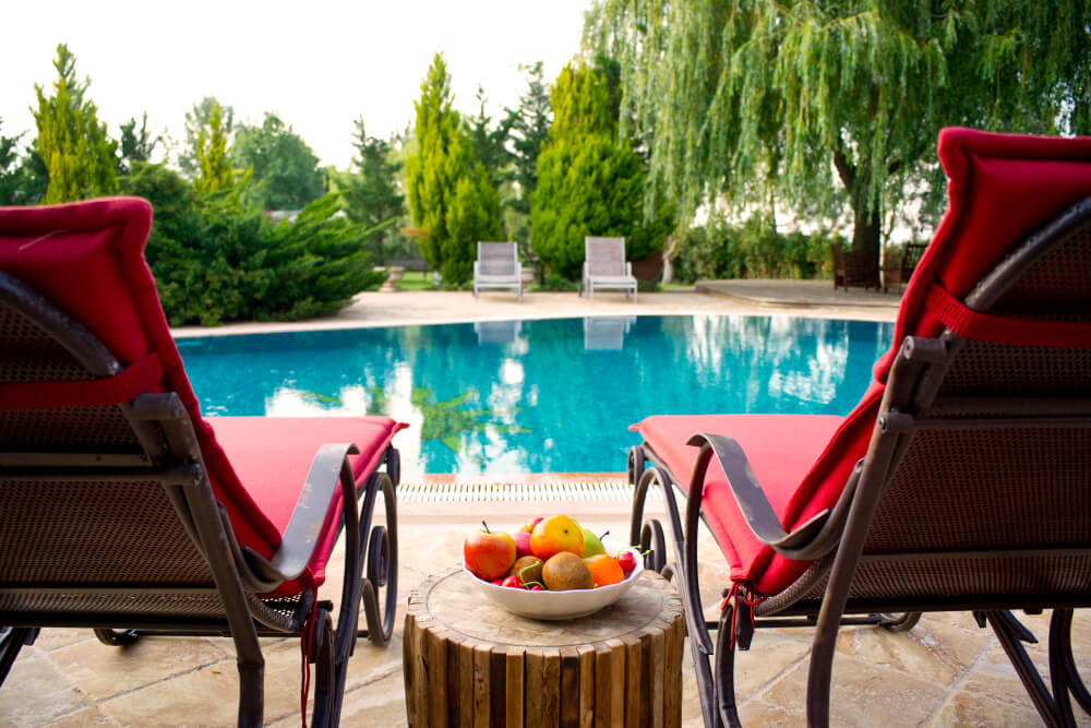 Two red lounge chairs overlooking a garden swimming pool