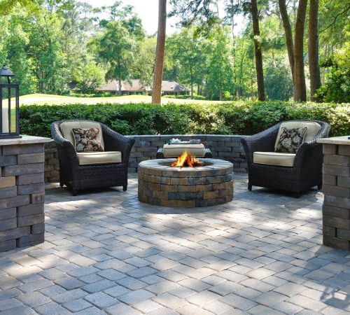 A beautiful outdoors pavers with two comfortable armchairs and a fire pit in a natural green environment